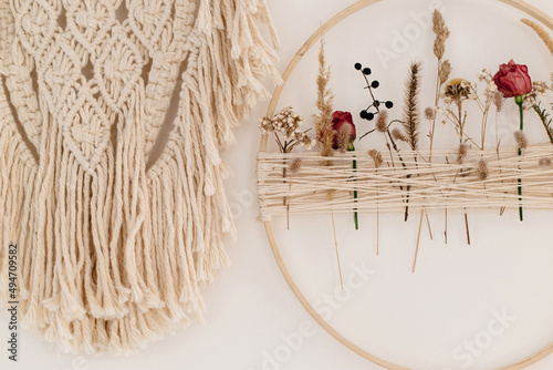 Stylish boho wreath with dry flowers and macrame hanging on white wall. Modern floral arrangement and creative handmade decor in modern boho room