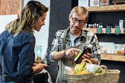 Принти на полотні Pretty young woman shopping while the seller advises on her purchases of organic food in a grocery store