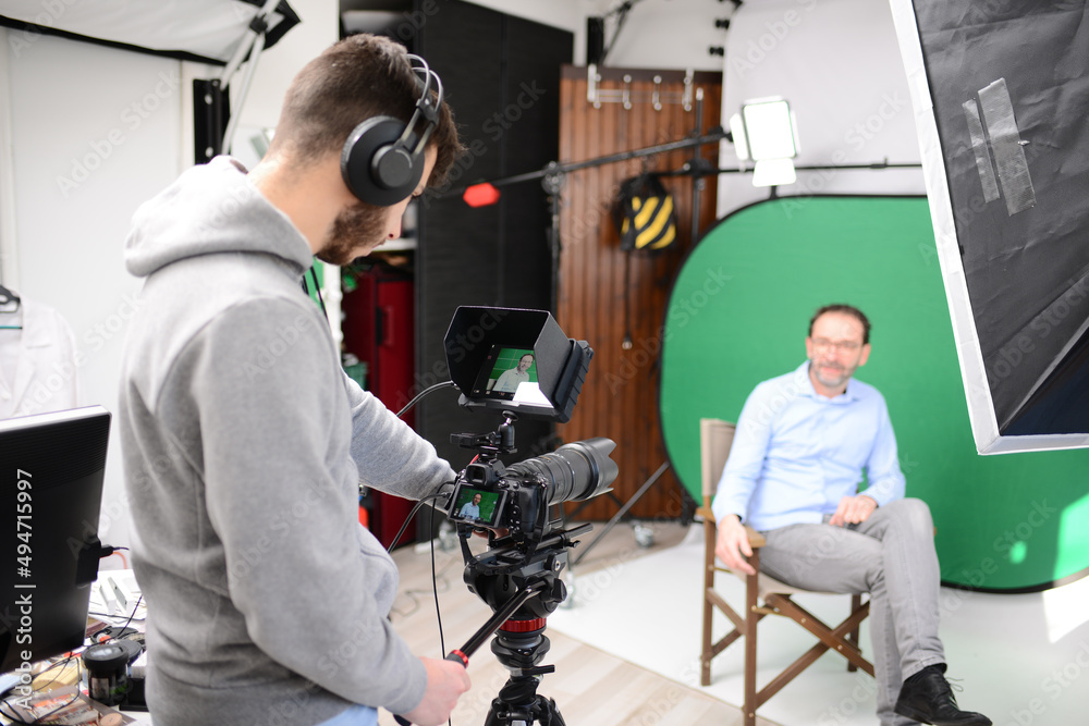 young man video camera operator making interview in professionnal broadcast tv movie studio film production with a green chromakey background young man video camera operator making interview in professionnal broadcast tv movie studio film production with a green chromakey background