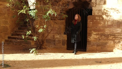 Young redhead girl admiring old gate on the ruins a monastery in Spain. XII-XIII century buiding of the christian monastic cluny order, female traveler. Woman exploring ancient ruins. photo