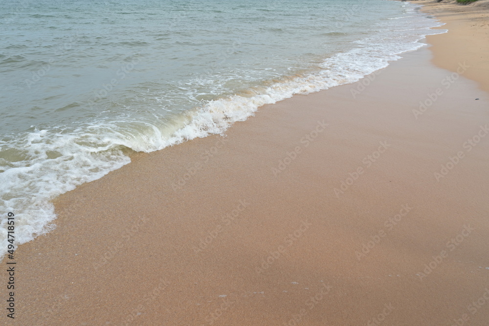 Scenery of waves hitting a sandy beach. White waves crash on the sandy beach in the summer morning. A beautiful sandy beach when the waves come.
