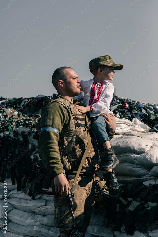 Ukrainian territorial defense warrior holds child boy in his hands on checkpoint.