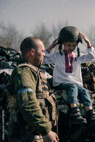Fototapeta Child boy sits on sandbags in checkpoint near Ukrainian territorial defense warrior