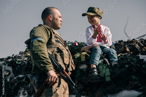 Child boy sits on sandbags in checkpoint near Ukrainian territorial defense warrior.