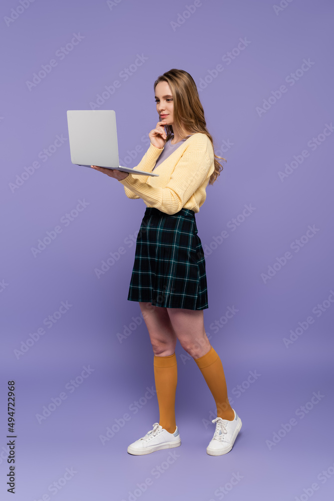 full length of young woman using laptop on purple. full length of young woman using laptop on purple.