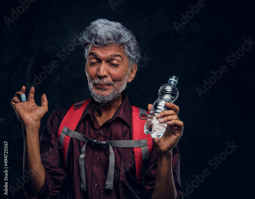 Old man tourist drinking water against dark background