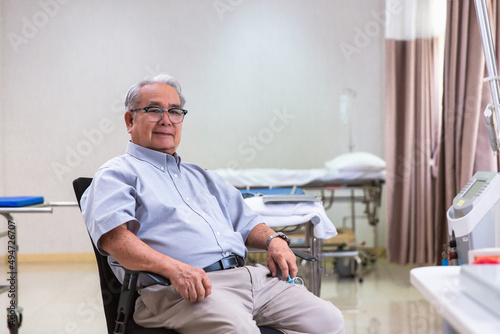 Happy optimistic senior 70s man looking at camera with smile during appointment at doctor office. Portrait of elder male patient in background. Medic care
