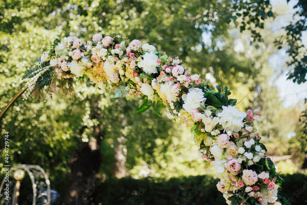 Obraz premium Details of the round wedding arch. Pink and white flowers, roses close-up, against a background of green trees in the park. 