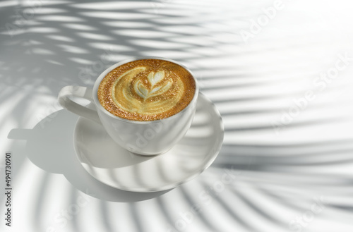 Latte art coffee on white background with palm leaves shadow. White on white and minimalist style.