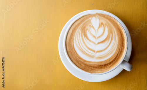 Top view of hot coffee with latte art on the yellow wooden background.