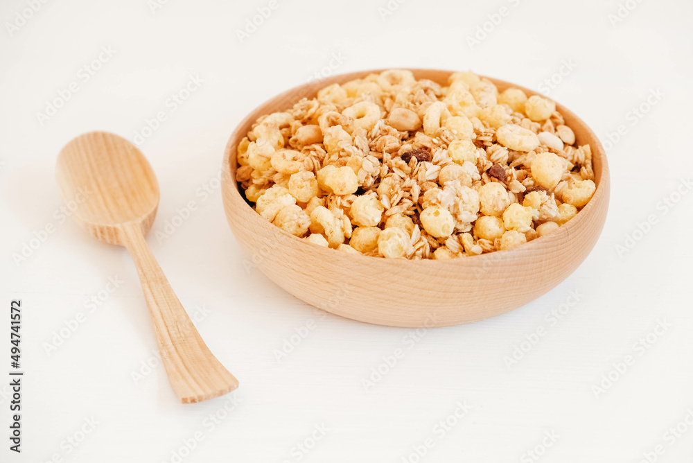 Dry muesli with cornflakes, nuts and raisins in a wooden bowl on a white background Dry muesli with cornflakes, nuts and raisins in a wooden bowl on a white background