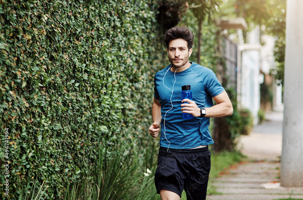 Just one more block to go. Shot of a sporty young man running running down a street while listening to music outside during the day.