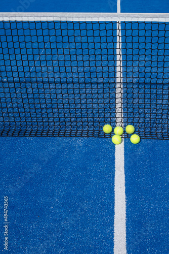 Five tennis balls by the net of a blue paddle tennis court, racket sports concept © Vic