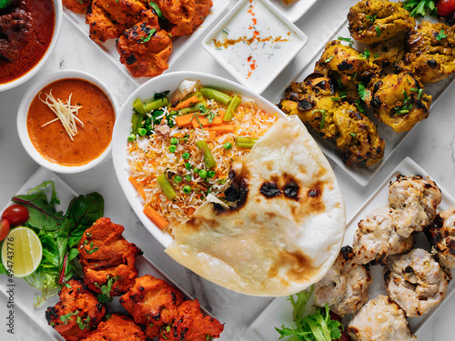 Assorted famous indian and pakistani food table vegetable biryani, Butter Chicken, paneer Chicken Tikka boti kebab, lime, Kali Mirchi, tomato sauce, raita, roti, salad, top view on grey background photo