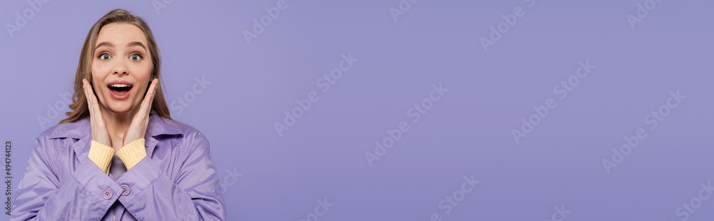 amazed young woman in violet rain coat looking at camera isolated on purple, banner amazed young woman in violet rain coat looking at camera isolated on purple, banner