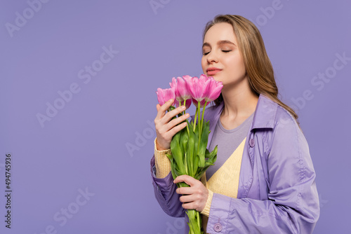young woman in trench coat smelling pink tulips isolated on purple.