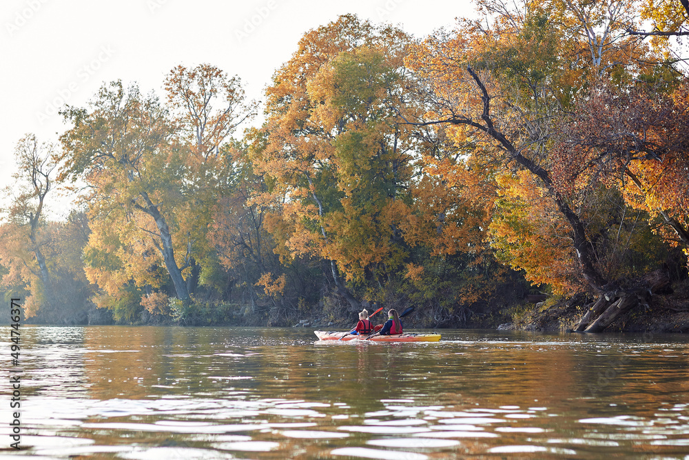 Two active women, best friends kayaking in a river at autumn season. Kayaking, travel, leisure concept Two active women, best friends kayaking in a river at autumn season. Kayaking, travel, leisure concept