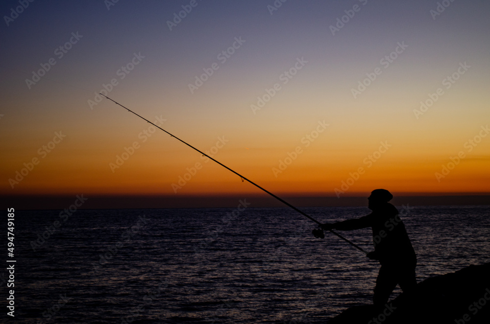 silhouette of a man fishing on the beach at sunset on a winter day
