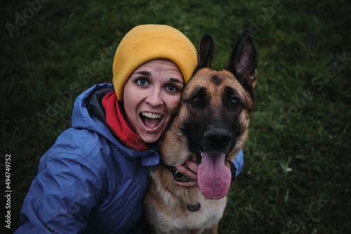 Have fun in park with furry human friend. Snow-white smile and tongue sticking out from joy. Young European white woman sits in green grass and hugs her German Shepherd dog top view.