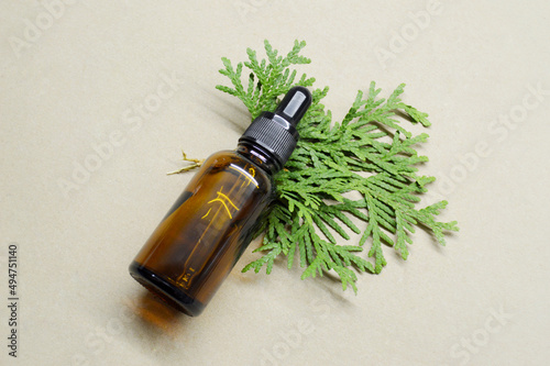 Empty brown glass bottle with pipette and leaf from juniper on craft background
