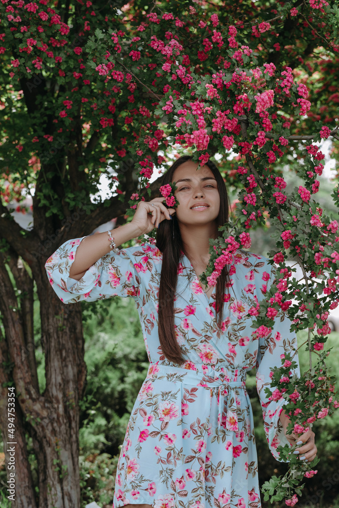 Attractive young Ukrainian woman stands under a flowering tree. Model smiling and posing for the camera with a flower in her hand. Attractive young Ukrainian woman stands under a flowering tree. Model smiling and posing for the camera with a flower in her hand.