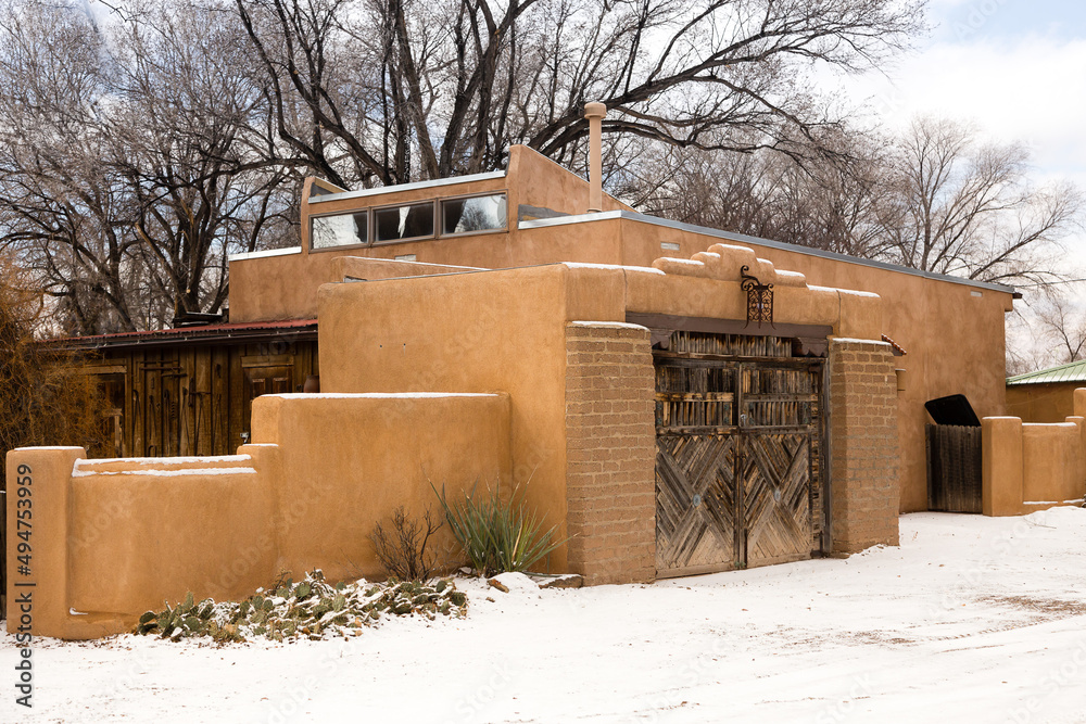 Fototapeta premium Traditional adobe building with southwest style wooden door seen from a street covered in rare fresh snow during an overcast winter day, Santa Fe, New Mexico, USA