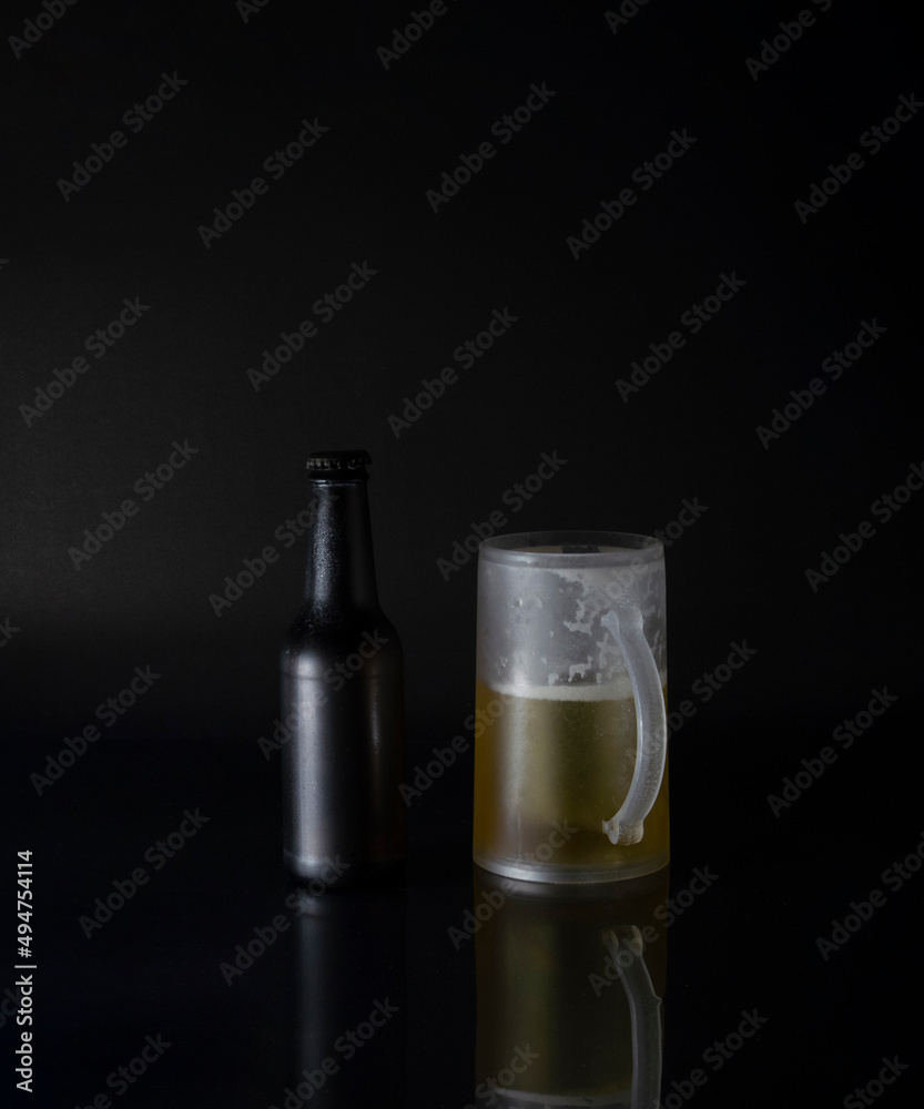 VIEW OF COLD BEER BOTTLE AND COLD BEER MUG ON A BLACK BACKGROUND VIEW OF COLD BEER BOTTLE AND COLD BEER MUG ON A BLACK BACKGROUND