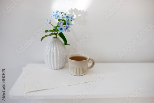 Flower hackelia velutina in a white fluted vase in the style of the seventies and a cup of coffee on the dresser. Scandinavian style