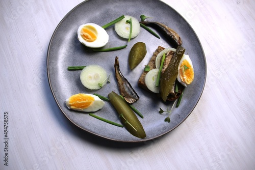 Plate with open sndwich with sprats, salty cucumber, onion, scallion, egg, bread on white background photo