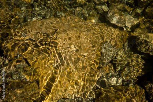 Vászonkép Golden sunlight patterns on riverbed rocks