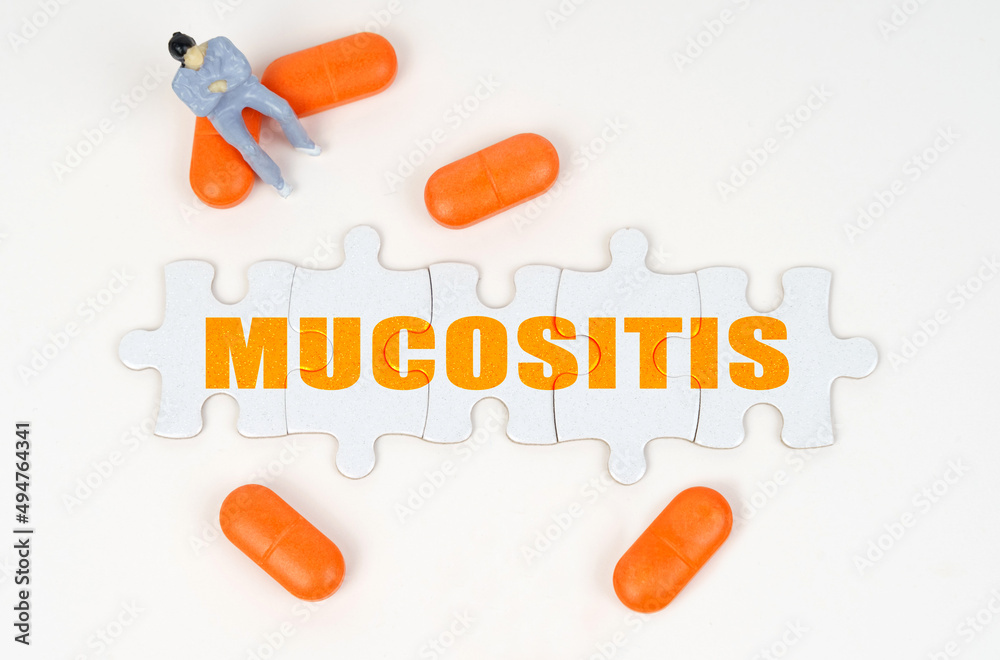 On the white surface of the tablet, a miniature human figure and puzzles with the inscription - Mucositis On the white surface of the tablet, a miniature human figure and puzzles with the inscription - Mucositis