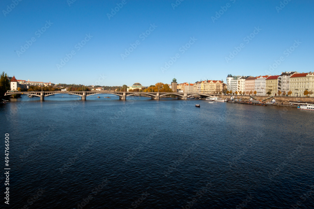 View of the theater district and the river on a sunny day and blue sky. View of the historic city center of Prague from a bank of the Vltava on a cloudless day. The sky is azure blue.