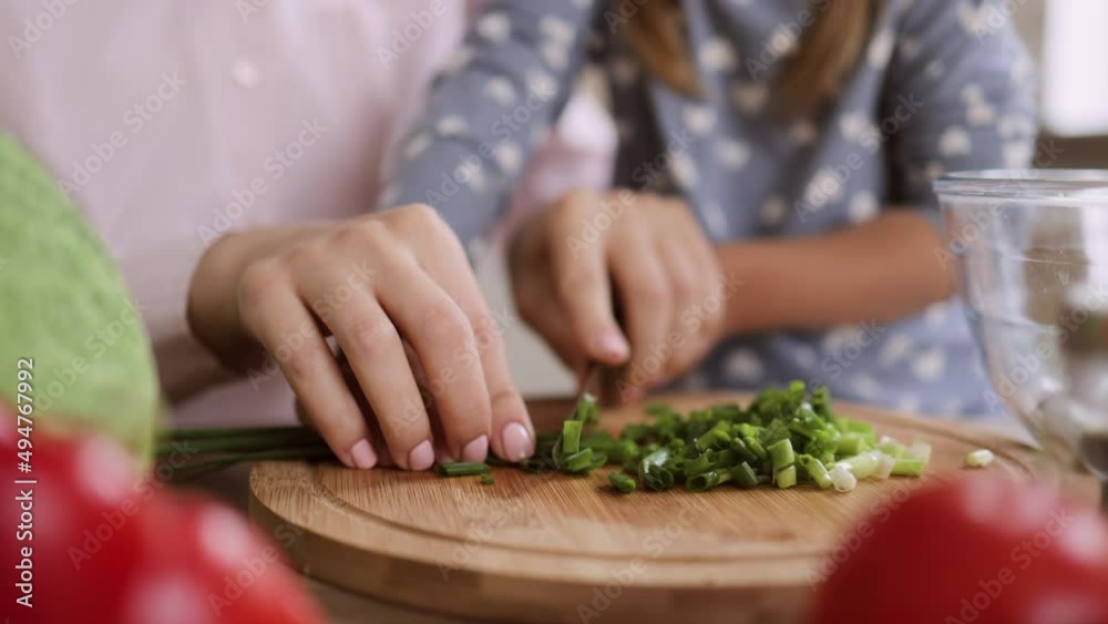 Close up of cute little girl and her beautiful mom in casual clothes are cutting onion and smiling while cooking in kitchen at home. Healthy food at home. Happy family in the kitchen. Close up of cute little girl and her beautiful mom in casual clothes are cutting onion and smiling while cooking in kitchen at home. Healthy food at home. Happy family in the kitchen.