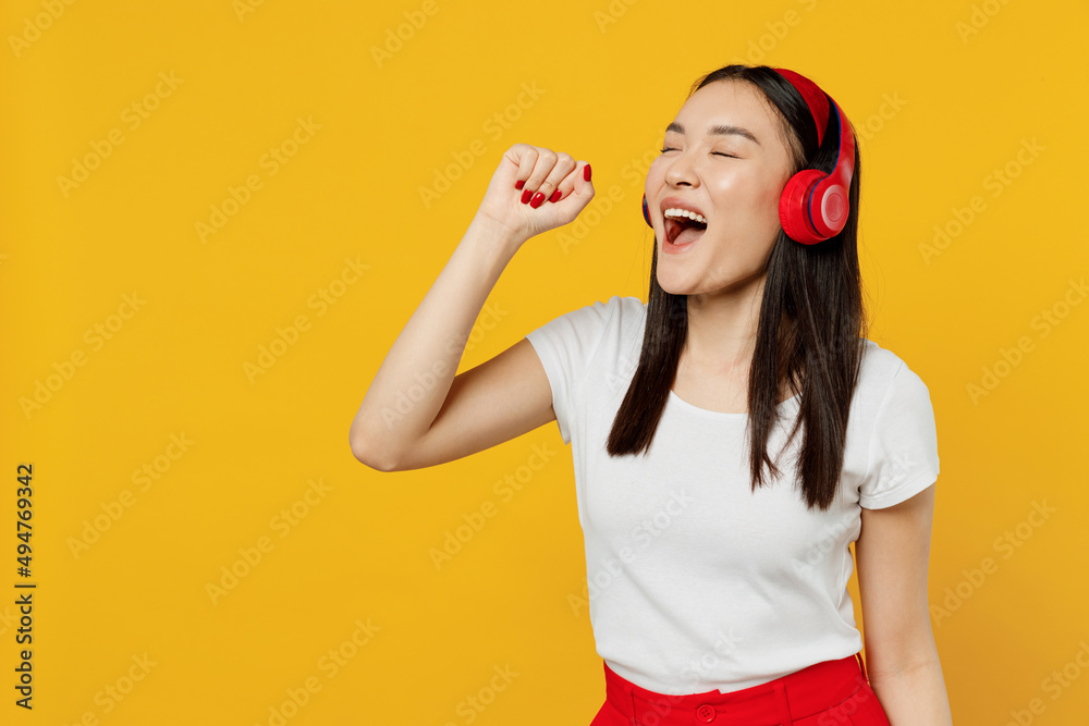 Excited delight young girl woman of Asian ethnicity 20s years old wear white t-shirt red headphones dance listen music sing in imaginary microphone isolated on plain yellow background studio portrait Excited delight young girl woman of Asian ethnicity 20s years old wear white t-shirt red headphones dance listen music sing in imaginary microphone isolated on plain yellow background studio portrait