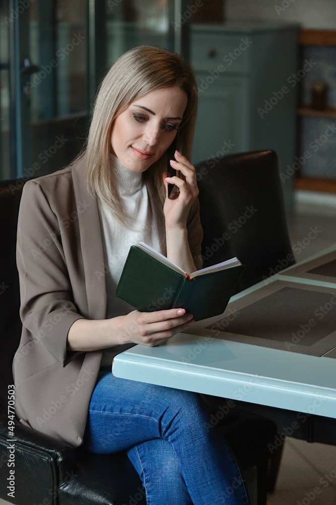 Obraz premium business beautiful self-confident woman sits at a table in a cafe waiting for an order and decides her working moments on the phone