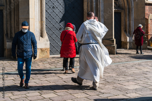 A priest in white robes speaks on the phone on the street of the old city while waiting for the ceremony to start at a safe distance from people during the covid pandemic © Александр Бочкала