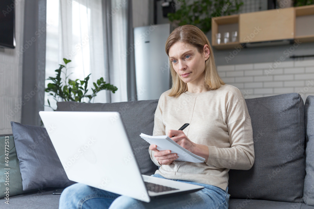 Woman at home studying online uses laptop sitting on sofa at home Woman at home studying online uses laptop sitting on sofa at home