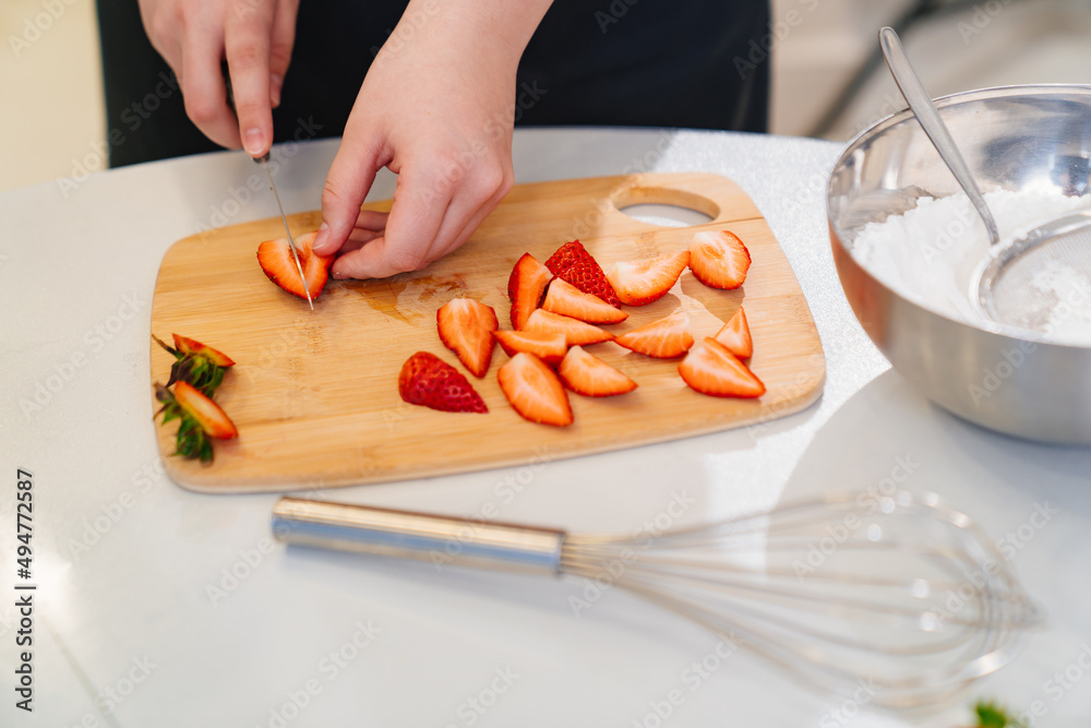 strawberries are cut into pieces on a wooden cutting board to decorate desserts.