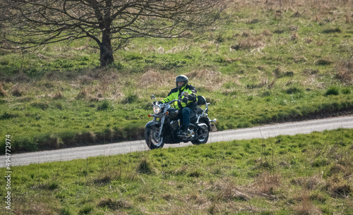 motorbike rider in a black and yellow high-vis jacket rides his Kawasaki Vulcan VN2000 motorcycle through spring countryside
