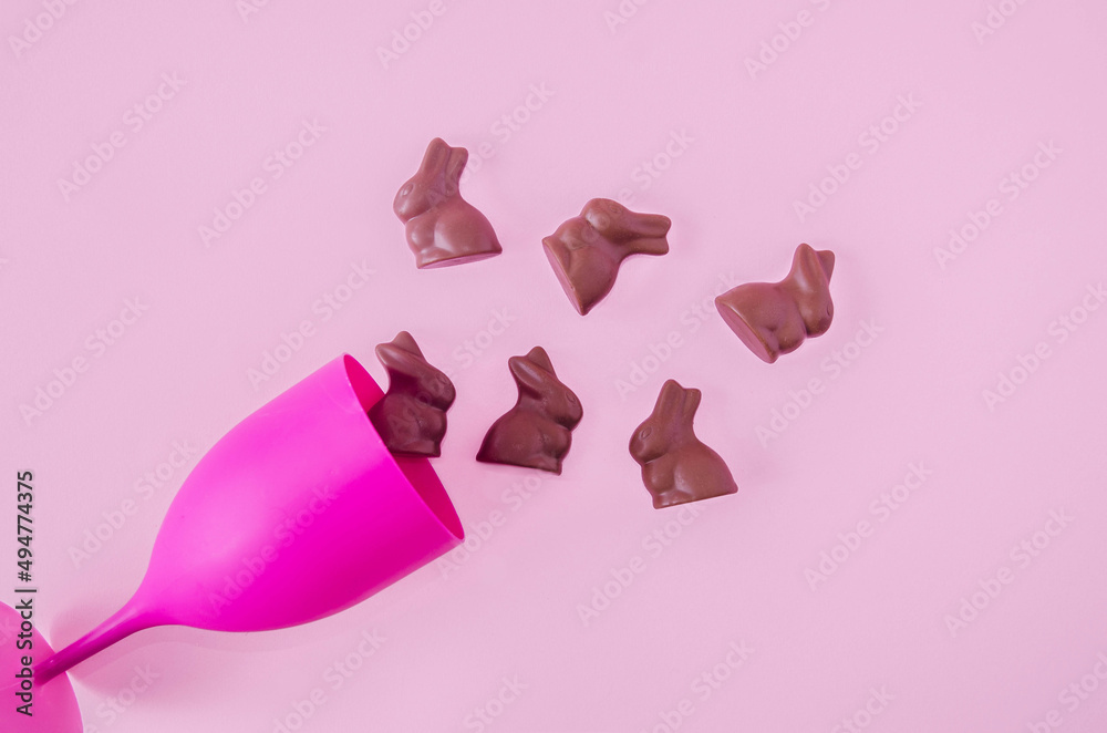 Chocolate bunnys going out of a fuchsia wine glass on pastel pink background. Surreal concept for Easter celebration banner or card.