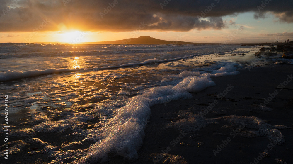 Sunrise over Rangitoto Island, sea foams catching sunlight at foreground, Takapuna Beach, Auckland.