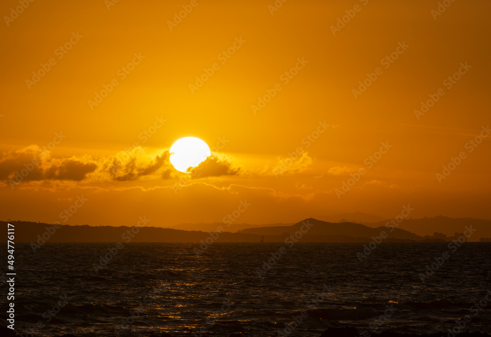 Sun rising over the clouds with distance hills in the horizon. Photo taken from Milford Beach, Auckland. Sun rising over the clouds with distance hills in the horizon. Photo taken from Milford Beach, Auckland.