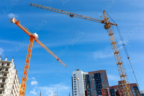 Two tower cranes on construction site against background of unfinished multi-storey buildings and blue sky photo