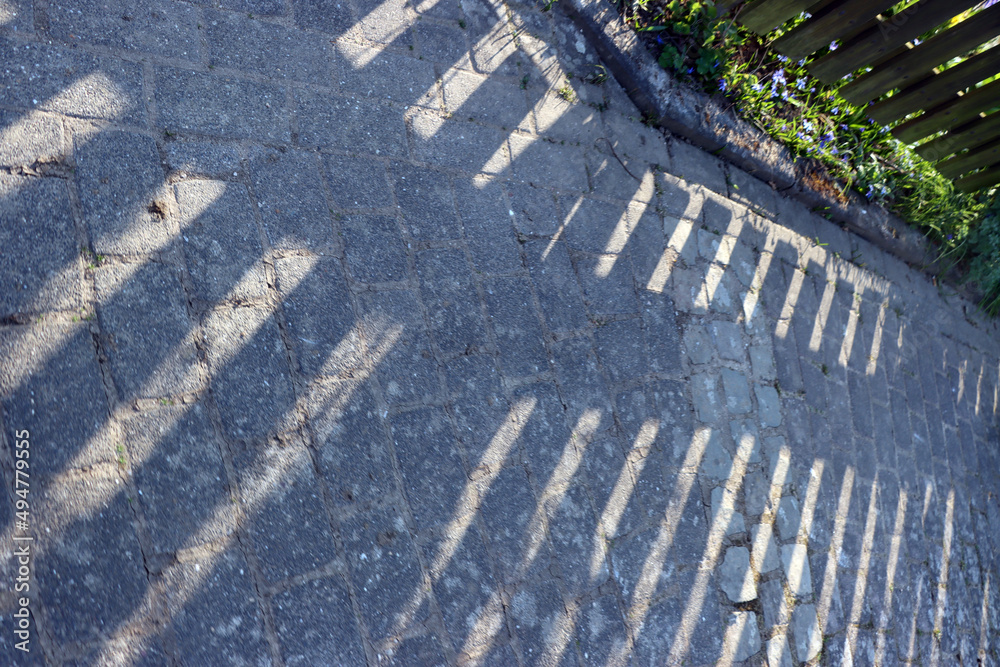 Holzzaum wirft einen Schatten auf das Strassenpflaster