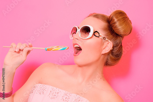 Portrait of stylish cute young blonde woman with colorful lollipop on pink background