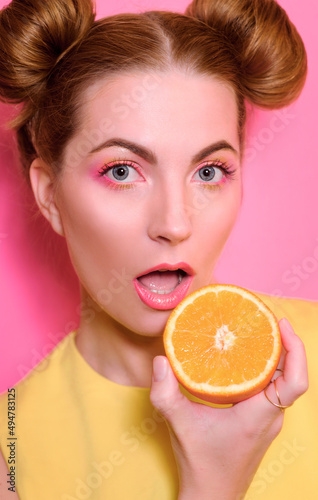 Portrait of stylish cute young blonde woman with oranges on pink background
