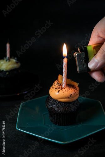 Chocolate Birthday cupcake with a single candle light on dark background.