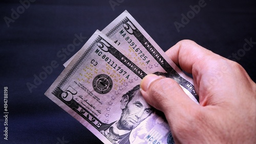 Businessman's hand holding American Dollar Banknotes, isolated on black background. Business Investment Economy Saving Loan Income Money and Finance concept. Five Dollar, 5 USD. Prosperity concept.