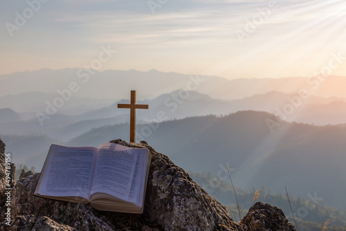 Leinwand Poster crucifix symbol and bible on top mountain with bright sunbeam on the colorful sk