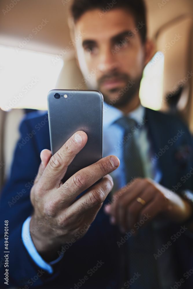 He needs his mobile phone on him at all times. Shot of a focused young businessman holding his cellphone while being seated in the back off a car. He needs his mobile phone on him at all times. Shot of a focused young businessman holding his cellphone while being seated in the back off a car.